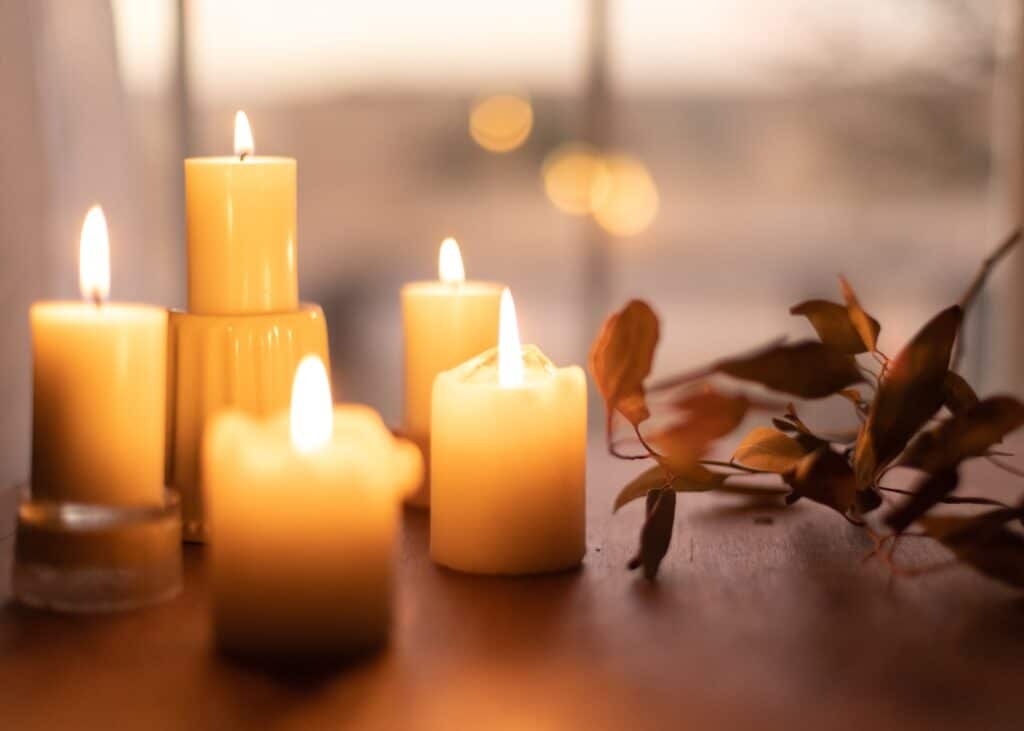 Photograph of four candles of various heights on a table with leaves nearby
