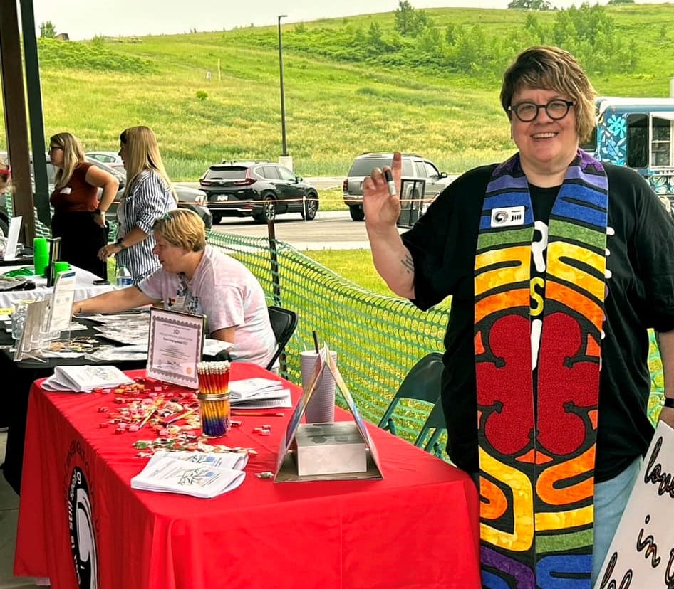 UCC pastor holds up glitter at Pride Festival table.