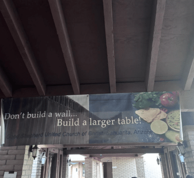 A sign reading, "Don't build a wall. . . Build a larger table!"