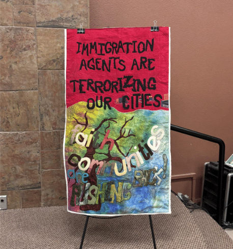 A colorful piece of quilted art is on a stage. It contains the words, "Immigration agents are terrorizing our cities. Faith communities are pushing back!"