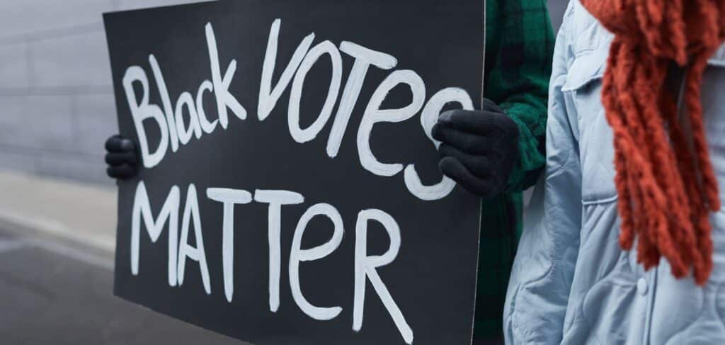 gloved hands holding a sign that reads Black Votes Matter