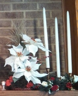 A white poinsettia and three white taper candles on an altar in front of a brick wall. 